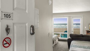 A hotel room with a view of the beach, a bed, a desk, and a no-smoking sign. - Oceanfront Ground Floor Studio  - Pool & Hot Tub! (Lincoln City)