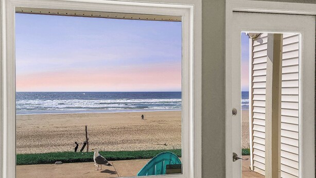 A view of a beach through a door, with a seagull and a person in the distance. - Oceanfront Ground Floor Studio  - Pool & Hot Tub! (Lincoln City)