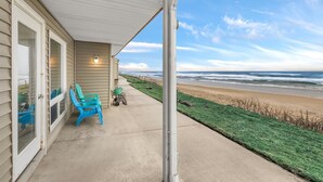 A beachfront property with a covered porch, two chairs, and a hose.