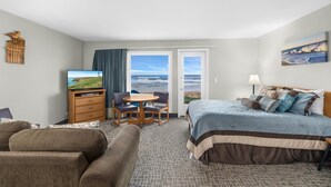 A hotel room with a bed, a desk, a chair, a television, and a view of the ocean.