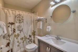 Een badkamer met douchegordijn met bloemenprint, toilet, wastafel met spiegel en een handdoekhouder.