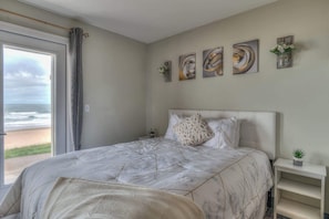 A bedroom with a large bed, a view of the beach, and four abstract paintings on the wall. - Ground Level Oceanfront Studio, Beach Access, Pool (Lincoln City)
