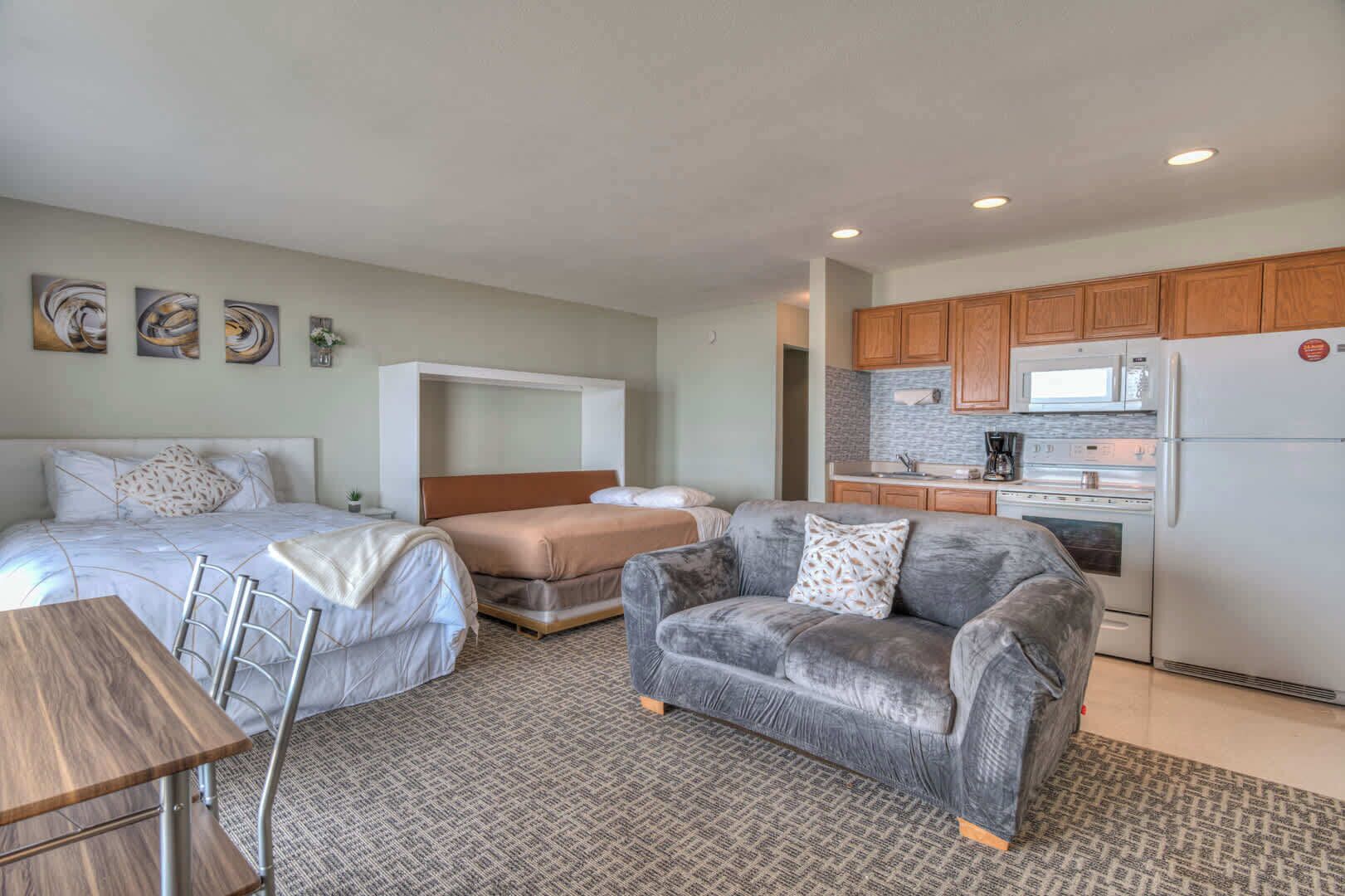 A compact hotel room with two beds, a kitchenette, and a seating area.