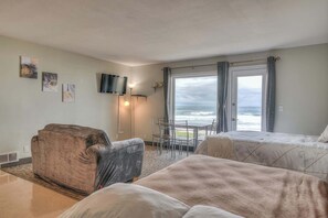 A hotel room with two beds, a sofa, a TV, and a view of the ocean.
