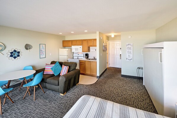 A compact living space with a kitchenette, a dining area with a table and chairs, and a sofa with colorful pillows.