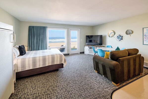 Een hotelkamer met een bed, een bureau met een televisie, een bank en uitzicht op het strand.