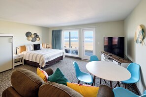 Une chambre d’hôtel avec un lit, une télévision, un coin repas avec des chaises et une vue sur la plage.