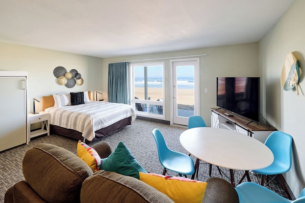 Ein Hotelzimmer mit Bett, Fernseher, Essbereich mit Stühlen und Blick auf den Strand.
