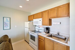 A compact kitchen with wooden cabinets, a refrigerator, microwave, stove, and a sink.