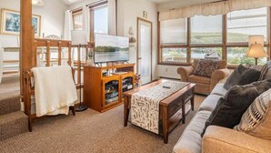 Ein gemütliches Wohnzimmer mit einer Holzbänkl, einem Fernseher, einer Couch und einem Fenster mit Blick.