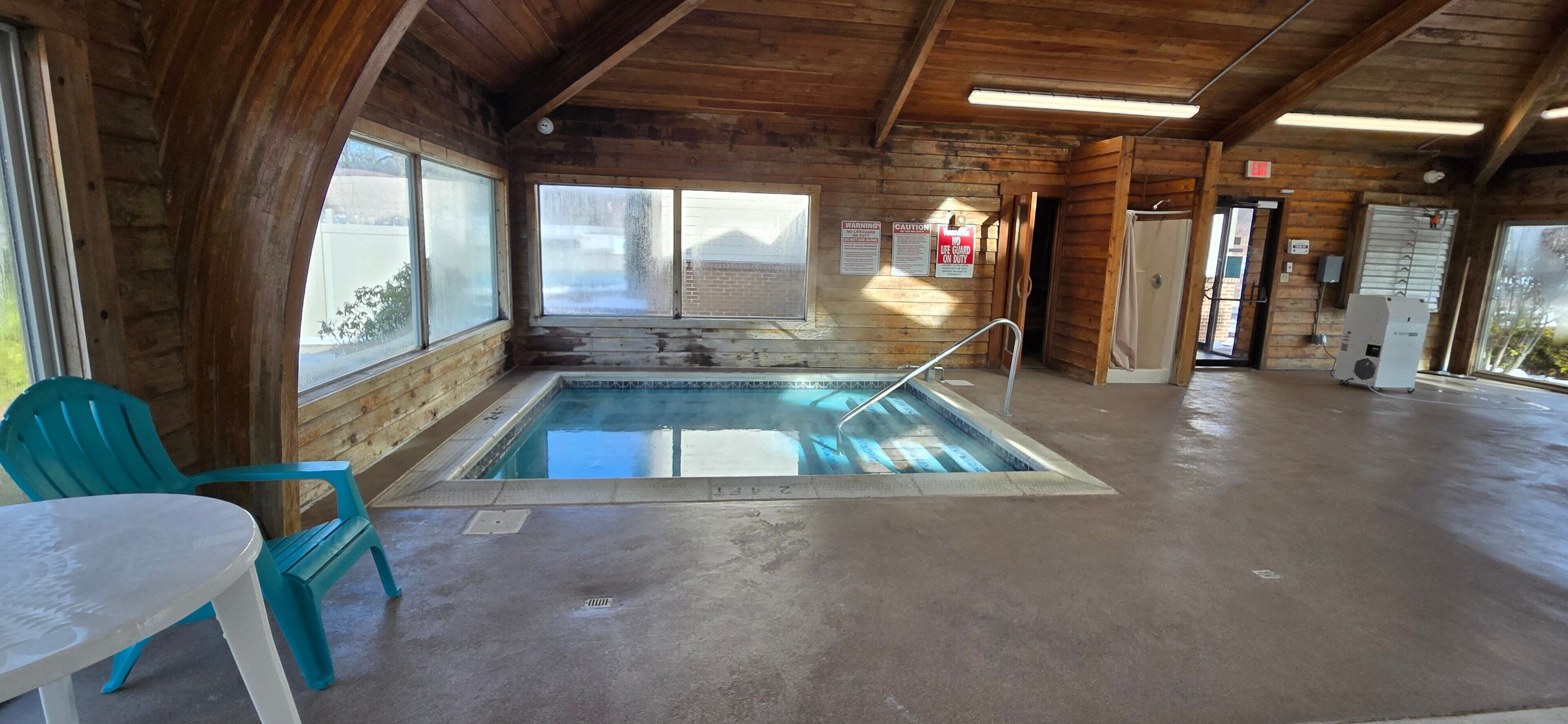 A wooden cabin with a small indoor pool, a table, and chairs.