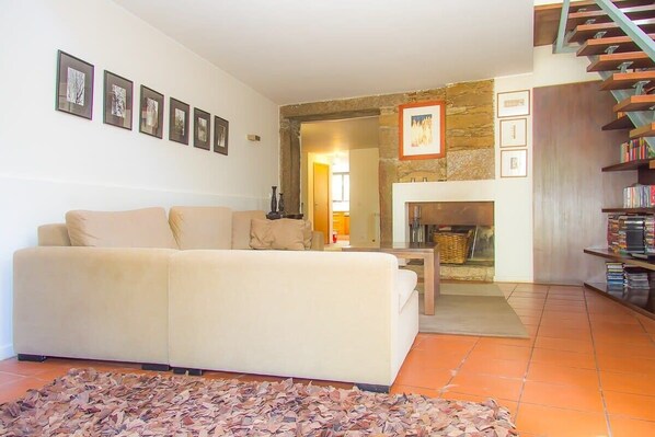 A living room with a sofa, a fireplace, a staircase, and framed pictures on the wall. - Liiiving in Caminha Oak Tree Chill House (Caminha)