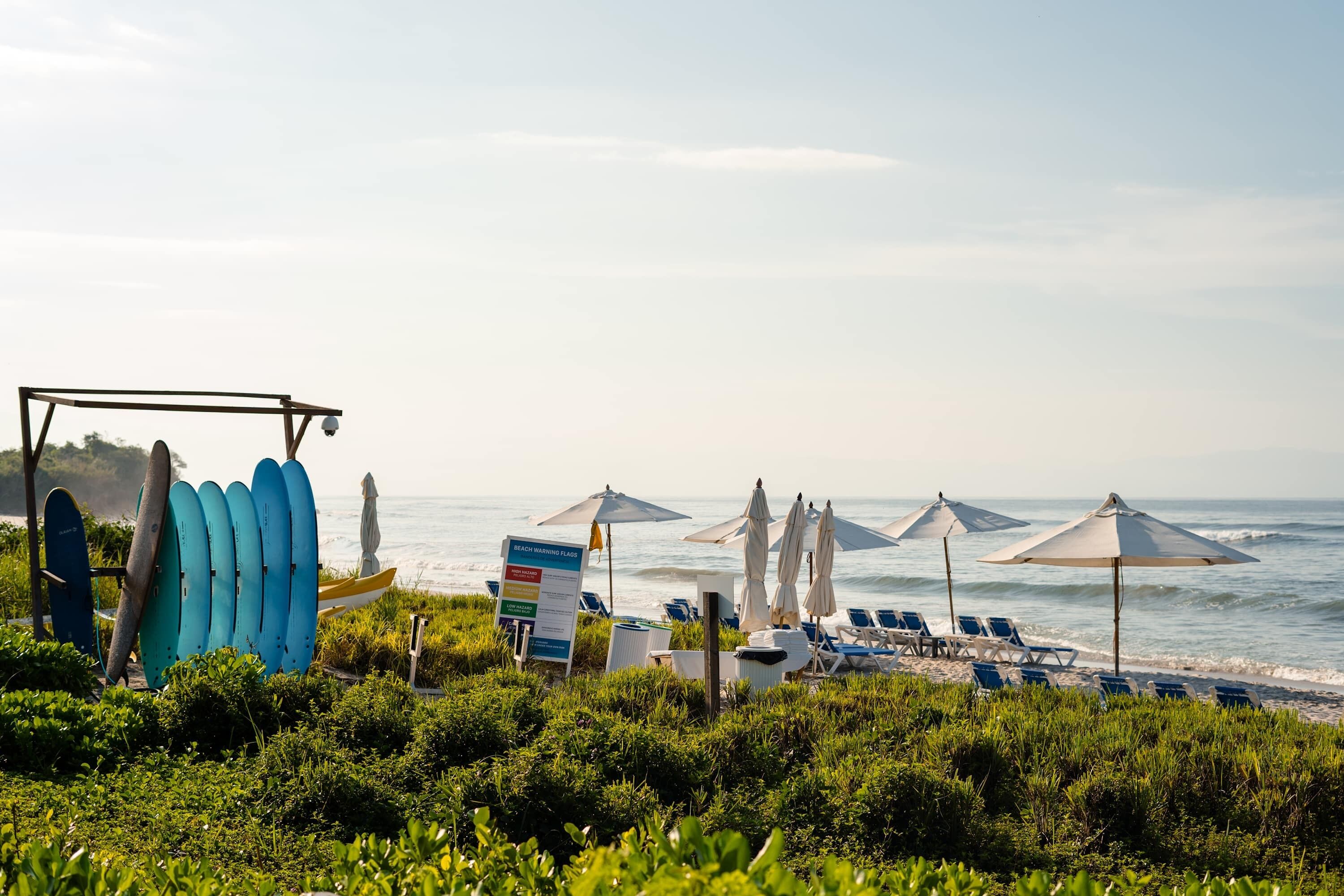 Una playa con tablas de surf, sombrillas y sillas reclinables.
