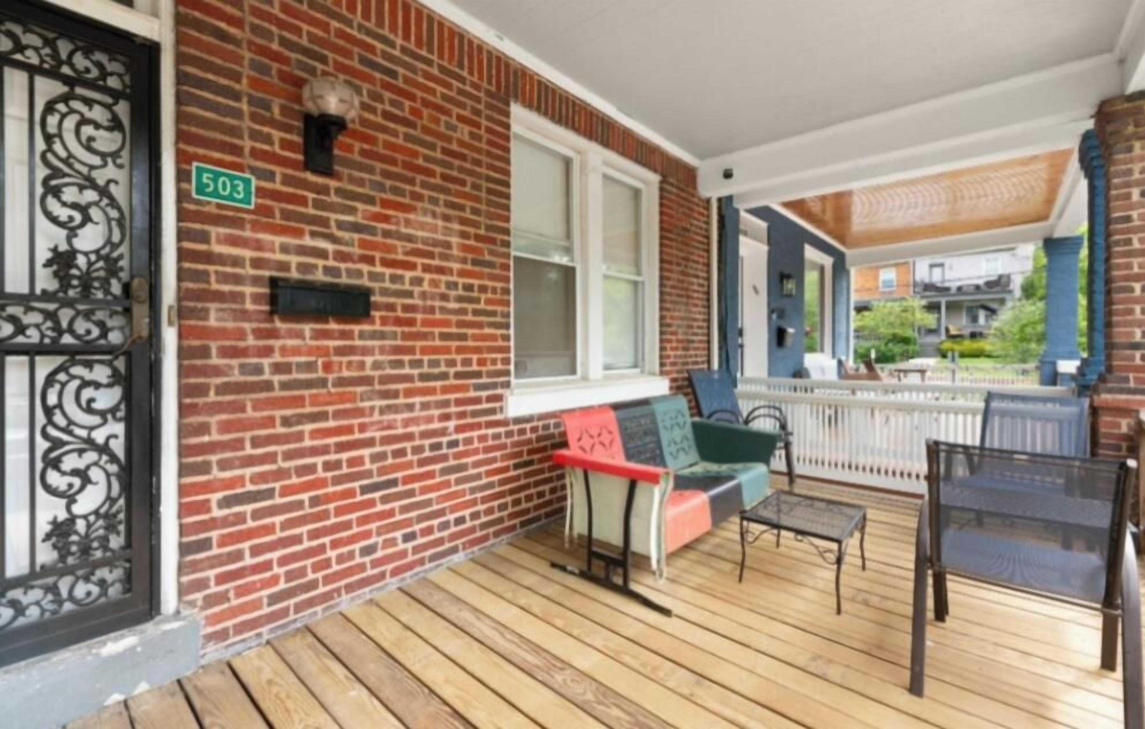 A brick house with a porch, a number 503 sign, a window, and a bench.