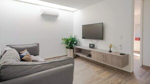 A modern living room with a sofa, a flat-screen TV mounted on the wall, a small plant, and a wooden cabinet. - Family Residencia Galicia (La Tijera)