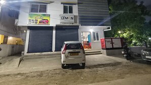 A multi-story building with two ground-floor garages, a car parked in front, and a sign for 'Lemon' on the ground floor. - Skyry Residency (Chennai)