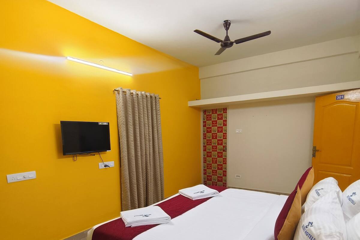 A hotel room with a bed, a desk, a television, and a ceiling fan.