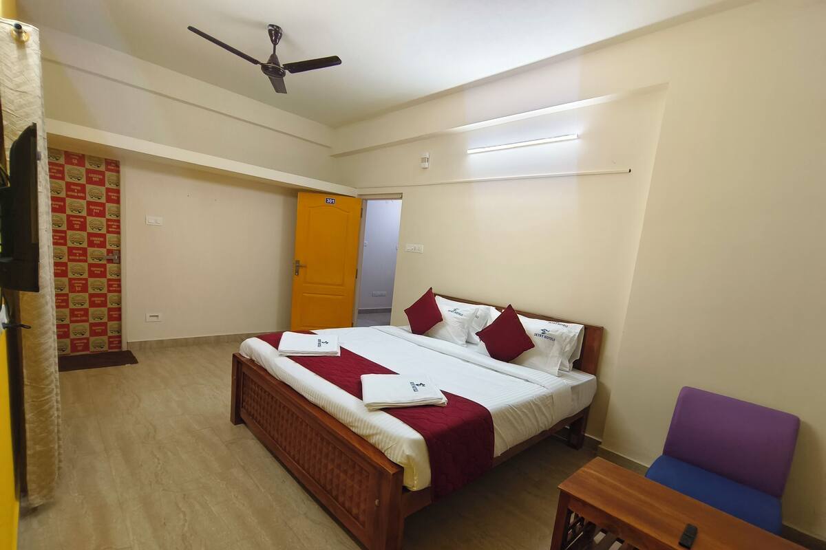 A hotel room with a bed, a chair, a small table, and a ceiling fan.