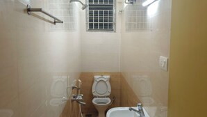 A small, compact bathroom with a toilet, sink, and shower. - Skyry Residency (Chennai)