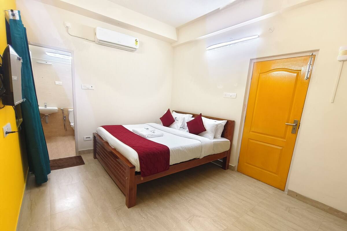 A bedroom with a bed, a bathroom visible through an open door, and a yellow door.