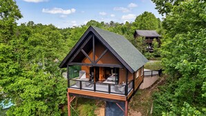 A wooden cabin with a balcony, surrounded by dense forest. - Romantic Couples Treehouse! Theatre! 3 min to PF! (Pigeon Forge)