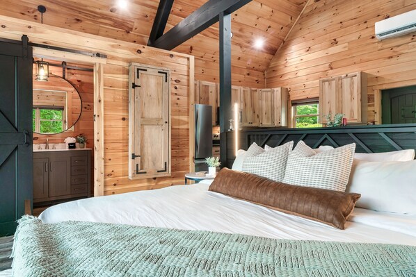 A wooden cabin bedroom with a bed, pillows, a nightstand, a mirror, and a window.