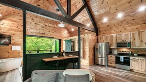 A cabin interior with a wooden ceiling, a dining area, a kitchen with modern appliances, and a view of the outdoors. - Romantic Couples Treehouse! Theatre! 3 min to PF! (Pigeon Forge)
