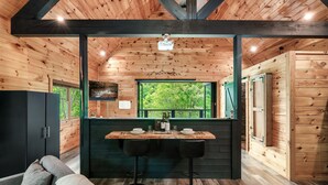 A wooden interior with a dining area, bar stools, and a TV mounted on the wall. - Romantic Couples Treehouse! Theatre! 3 min to PF! (Pigeon Forge)