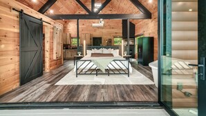 A log cabin interior with a large bed, wooden walls, and a glass door leading outside. - Romantic Couples Treehouse! Theatre! 3 min to PF! (Pigeon Forge)