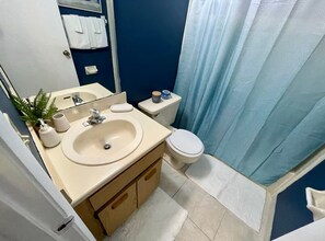 Een badkamer met een beige wastafel, een wit toilet en een blauw douchegordijn.
