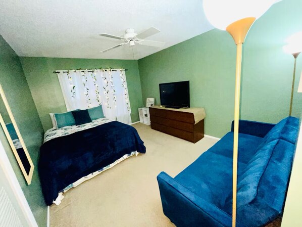 A bedroom with a bed, a blue sofa, a dresser, a television, and a ceiling fan.