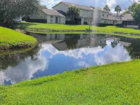 A residential area with a pond reflecting a house and a clear sky.