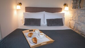 Un lit bien fait, recouvert d’une couverture sombre, avec deux oreillers et un plateau contenant des croissants et des tasses de café.