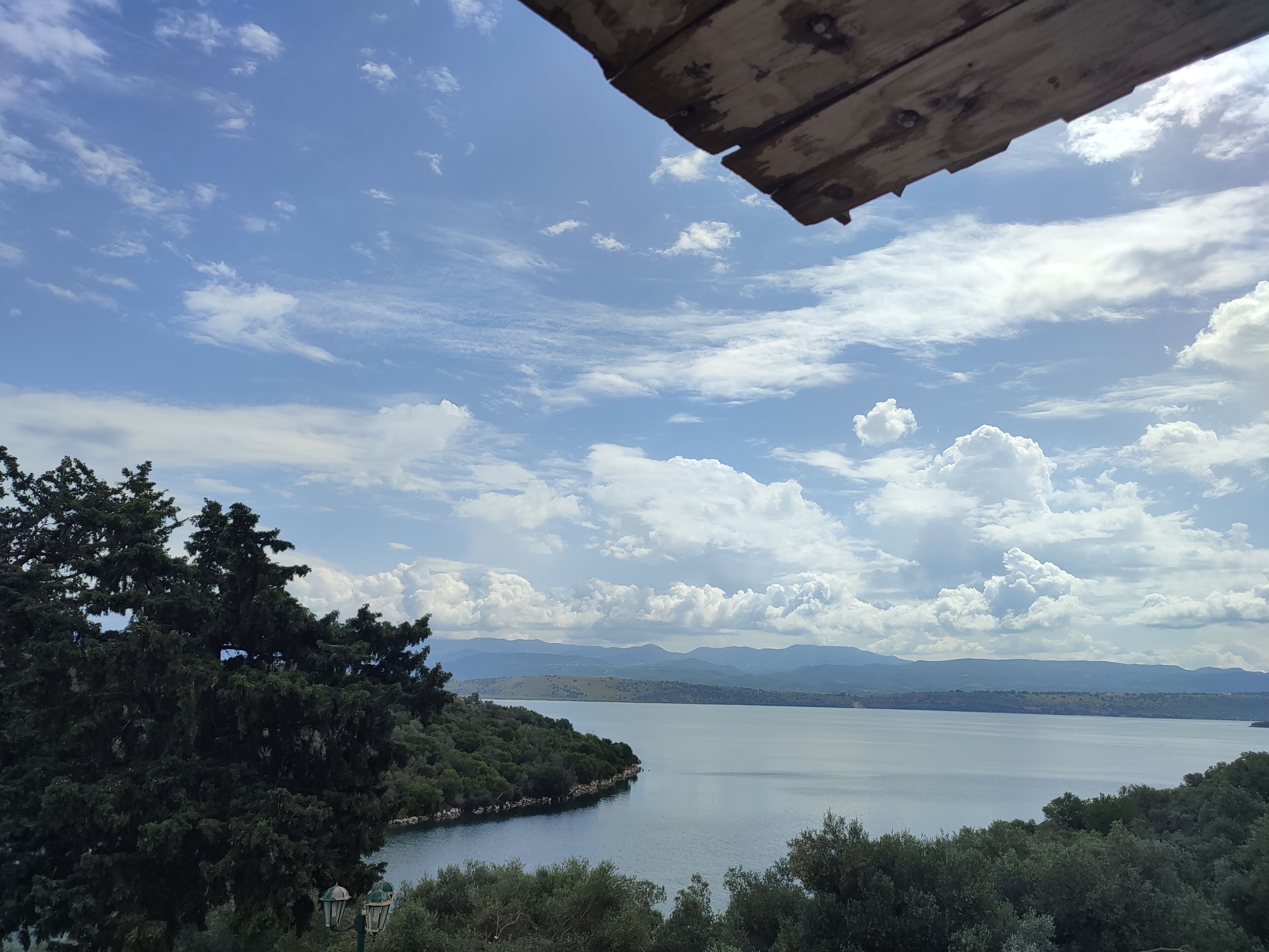 A view of a lake with a wooden structure overhead, surrounded by dense trees and distant mountains.