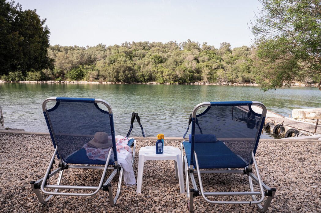 Two beach chairs facing a lake with a forested hillside in the background.