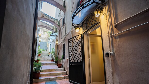 Une ruelle étroite avec un portail noir, des plantes en pot et un escalier menant à l’entrée d’un immeuble.