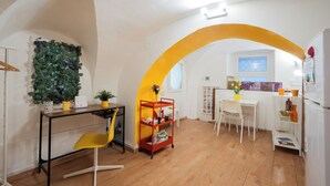 Une cuisine compacte avec un plancher en bois, un coin repas avec une table et des chaises blanches, et une plante fixée au mur.