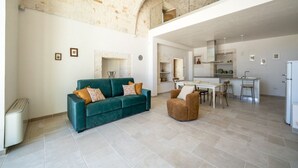 A spacious living area with a sofa, a chair, a dining table, and a kitchen in the background. - Palmento Giorgio Suite – authentic rural home in Puglia (Martina Franca)