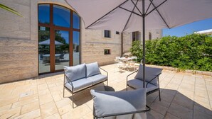An outdoor patio with stone flooring, a large umbrella, and two grey cushioned chairs. - Palmento Giorgio Suite – authentic rural home in Puglia (Martina Franca)