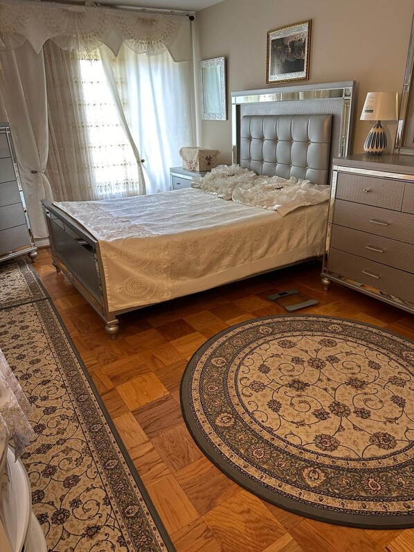 A bedroom with a bed, a dresser, a nightstand, a mirror, and a round rug.