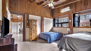 Una habitación con paredes de madera, un ventilador de techo, una cama, un televisor y un armario.