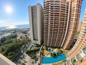 A high-rise building with multiple balconies, a swimming pool, and a view of the surrounding cityscape.