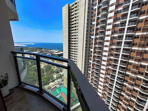 A high-rise building with multiple balconies, a clear view of the ocean, and a parking area below.