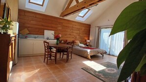 A cozy room with a wooden ceiling, a dining area with a table and chairs, a bed with a red blanket, and a large window. - Studio with terrace and garden 15 minutes from Guédelon (Treigny-Perreuse-Sainte-Colombe)