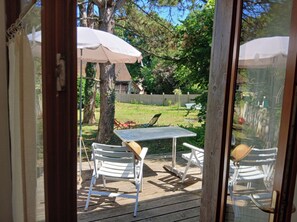 A wooden deck with a table and two chairs, an umbrella, and a view of a backyard with a lawn and trees.