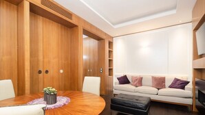 Ein modernes Wohnzimmer mit einem Holzkabinett, einem runden Esstisch mit Stühlen, einer Couch mit Kissen und einem Fernseher.