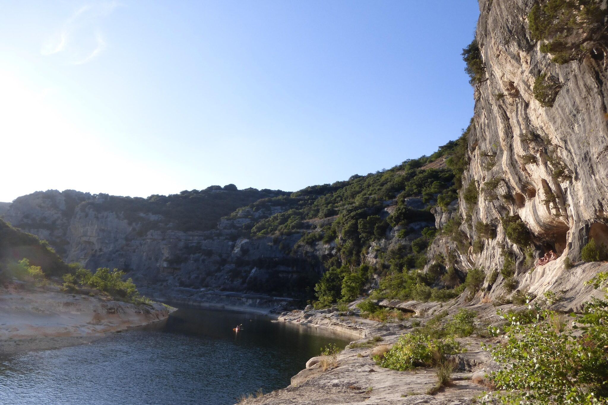A coastal landscape with a rocky cliff, a calm body of water, and greenery.
