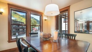 A dining area with a wooden table, chairs, and a large window with a view of a mountain and buildings. - 204 Ballard N-Curate Telluride, Town Center, Near Gondola, Parking, Partial AC (Telluride)