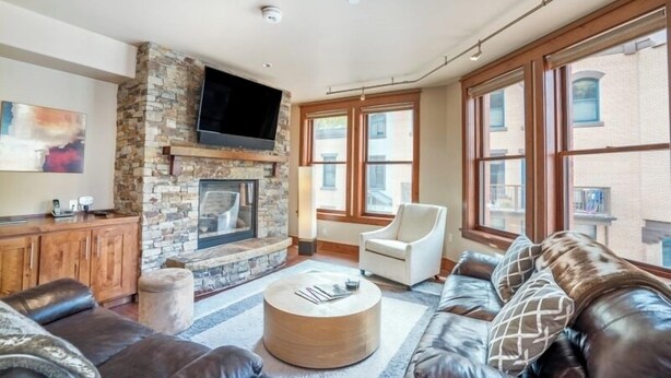 A living room with a stone fireplace, leather sofa, and large windows. - 204 Ballard N-Curate Telluride, Town Center, Near Gondola, Parking, Partial AC (Telluride)