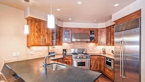 A modern kitchen with wooden cabinets, a stainless steel refrigerator, and a granite countertop island. - 204 Ballard N-Curate Telluride, Town Center, Near Gondola, Parking, Partial AC (Telluride)